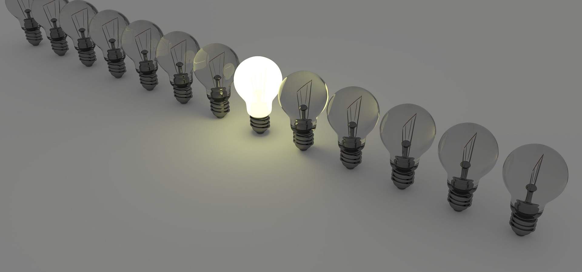 Line of lightbulbs that are standing upright on a table. A single lightbulb in the center is lit.